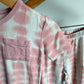 Pink and white tie-dye short-sleeve pajama top with a chest pocket, hanging on a wooden hanger next to matching tie-dye pants.